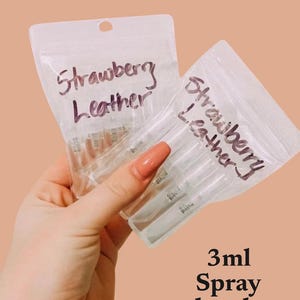 May include: A clear plastic bag filled with small, clear glass spray bottles. The bottles are labeled "Strawberry Leather" in black marker. The bag is held in a hand. The text "3ml Spray Bottle" is written below the image.
