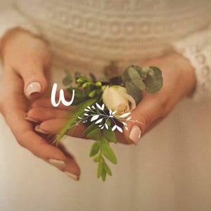 Puede incluir: Un prendedor floral que presenta un capullo de rosa de color crema, hojas de eucalipto verdes y pequeñas ramitas de follaje. El arreglo está acentuado con un logotipo gráfico blanco que consiste en la letra W y un diseño de hoja estilizado.