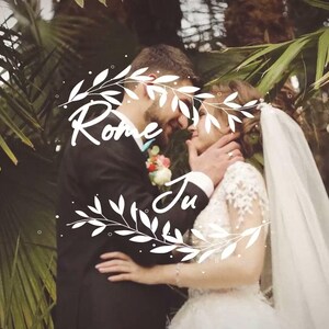 Puede incluir: Una pareja con ropa de boda se abraza entre grandes hojas de palmera verdes. La persona de la izquierda lleva un traje oscuro con un prendido floral, la de la derecha un vestido de encaje blanco y velo. Texto blanco dice Rome Ju.