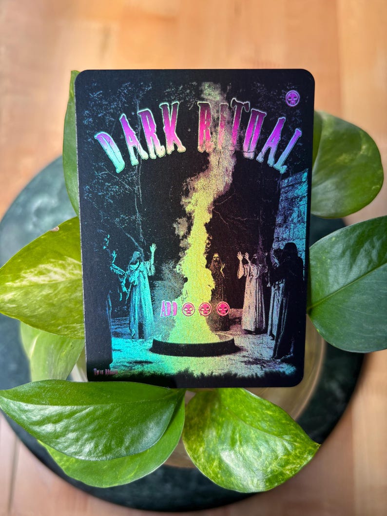 Pode incluir: Um cart&atilde;o preto com as palavras "DARK RITUAL" em letras iridescentes. A imagem mostra figuras em vestes em volta de um caldeir&atilde;o com uma chama colorida. O cart&atilde;o tem um acabamento hologr&aacute;fico.