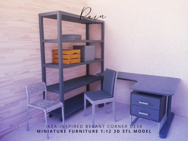 K&ouml;nnte beinhalten: Ein Miniaturmodell im Ma&szlig;stab 1:12 eines Ecktisches mit Schublade, inspiriert vom IKEA Bekant Schreibtisch. Der Schreibtisch ist aus grauem Karton und wird von einem grauen Metallregalsystem mit einer gelben Holzkiste und einer grauen Kiste auf den Regalbrettern begleitet. Der Schreibtisch wird au&szlig;erdem von zwei grauen St&uuml;hlen begleitet.
