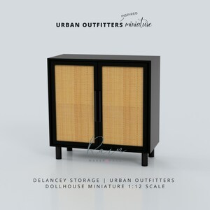 May include: Black cabinet with two doors and woven cane panels. The cabinet is on small black legs. The text "INSPIRED URBAN OUTFITTERS miniature" is above the cabinet. The text "DELANCEY STORAGE | URBAN OUTFITTERS DOLLHOUSE MINIATURE 1:12 SCALE" is below the cabinet.