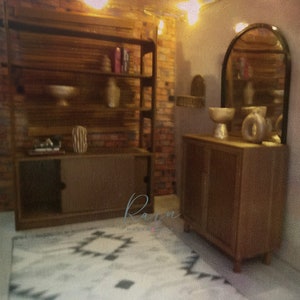 May include: A wooden cabinet with two doors and a shelf, a wooden shelf unit with four shelves, a white and gray patterned rug, and a large arched mirror with a gold frame. The cabinet and shelf unit are both in a rustic style.