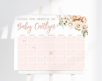 以下が含まれることがあります： 金とピンクの文字で「GUESS THE ARRIVAL OF Baby Caitlyn」と書かれた長方形の看板。右上には花の装飾があり、4月と5月のカレンダーグリッドには淡いピンク色の四角い枠が配置されています。