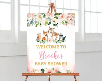 May include: Welcome to Brooke's Baby Shower sign with a pink and gold floral design. The sign features a deer, fox, owl, and raccoon surrounded by flowers.