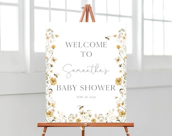 Op de afbeelding: Welkom op Samantha's Baby Shower bord met een bloemige rand en bijen. Het bord is wit met zwarte tekst en een datum van 28 juni 2023.