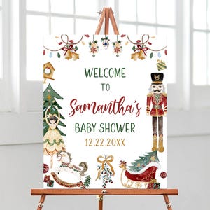 May include: A white sign on a wooden easel with a Christmas-themed baby shower design. The sign reads "Welcome to Samantha's Baby Shower 12.22.20XX" in green and red text. The design includes illustrations of a nutcracker, ornaments, and a rocking horse.