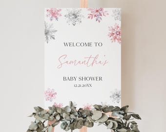 May include: A baby shower welcome sign on an easel. The sign is white with pink and gray snowflake accents. The text reads "Welcome to Samantha's Baby Shower 12.21.20XX."