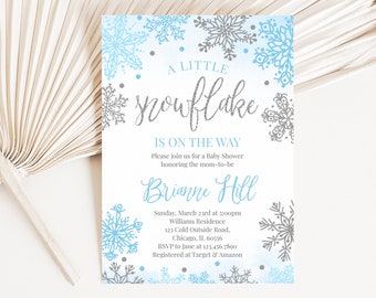 May include: A baby shower invitation with a winter theme. The invitation features a watercolor background with blue and gray snowflakes. The text reads "A Little Snowflake Is On The Way" in silver glitter.