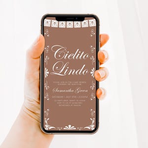 May include: A smartphone displaying a digital baby shower invitation on a brown background. The text reads Cielito Lindo, Please join us for a baby shower honoring the mom to be, Samantha Green, Saturday, July 9th, 2:00PM, 123 Party Drive, Trinity, NY, 10006, RSVP to Gia at 123-456-7890, Registered at Amazon. White decorative borders frame the top and bottom.