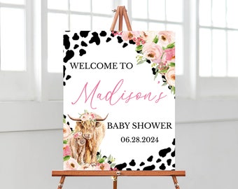 Puede incluir: Un letrero de bienvenida para un baby shower sobre un caballete. El letrero presenta una ilustración de acuarela de una vaca de las Tierras Altas y su ternero, rodeados de flores rosas y blancas. El texto dice "Bienvenida a la fiesta de bienvenida de Madison 06.28.2024".