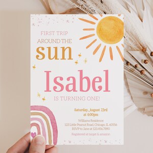 Pu&ograve; includere: Un invito di primo compleanno rosa e oro con un design a tema sole e arcobaleno. L'invito recita "Primo viaggio intorno al sole Isabel compie un anno!" e include i dettagli della festa, tra cui data, ora, luogo e informazioni RSVP.