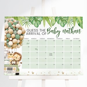 May include: A rectangular sign featuring a calendar for April and May with the text GUESS THE ARRIVAL OF Baby nathan. It displays a green safari jeep with cartoon animals and a large cluster of beige, white, and sage green balloons.