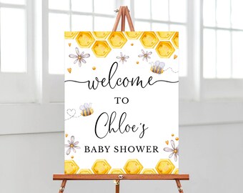 May include: Welcome to Chloe's Baby Shower sign featuring a honeycomb pattern, bees, and flowers. The sign is white with black text.