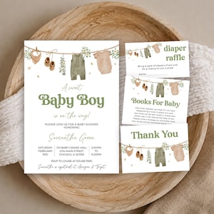 May include: A baby shower invitation set featuring watercolour illustrations of baby clothes on a clothesline, including a bib, booties, and onesies in olive green and beige. The text includes A sweet Baby Boy is on the way, Diaper Raffle, and Thank You.