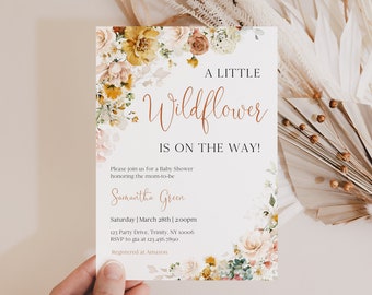 Op de afbeelding: Een witte babyshower-uitnodiging met een aquarelbloemendesign in tinten geel, oranje, roze en groen. De tekst luidt "A Little Wildflower is on the Way!" en bevat de naam "Samantha Green", de datum en tijd van de babyshower, en het adres. De uitnodiging bevat ook de tekst "Registered at Amazon".