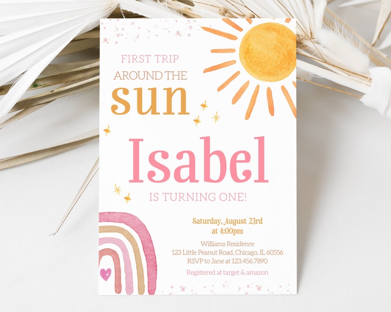 Pu&ograve; includere: Un arcobaleno acquerellato rosa e arancione con un cuore bianco al centro. Il testo "FIRST TRIP AROUND THE sun Isabel IS TURNING ONE!" &egrave; stampato in oro e rosa. L'invito &egrave; per una festa di primo compleanno il 23 agosto alle 16:00. L'indirizzo, le informazioni RSVP e i dettagli del registro sono inclusi.