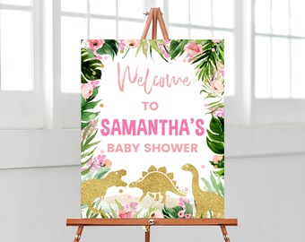 Könnte beinhalten: Willkommen zur Babyparty von Samantha Schild mit pinkfarbenem und goldenem Glitzertext, tropischen Blättern und rosa Blüten. Zwei goldene Glitzer-Dinosaurier befinden sich am unteren Rand des Schildes.