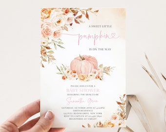 May include: Baby shower invitation with a watercolor design. The invitation features a pink pumpkin, floral accents, and the text "A sweet little pumpkin is on the way." The invitation is held by a hand.