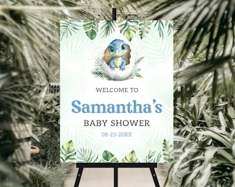 May include: A baby shower welcome sign featuring a blue dinosaur hatching from an egg, surrounded by green leaves. The sign reads "Welcome to Samantha's Baby Shower" with the date 08-23-20XX. The sign is displayed on a black easel.