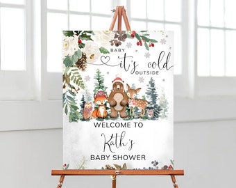 May include: A welcome sign for a baby shower, featuring watercolor illustrations of woodland animals and winter foliage. The sign reads "Baby, it's cold outside" and "Welcome to Kath's Baby Shower."