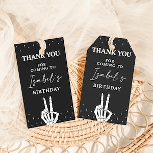 May include: Two black gift tags with the text "THANK YOU FOR COMING TO Isabel's BIRTHDAY". Each tag features a white skeleton hand making a peace sign. The tags are tied with twine.