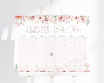 以下が含まれることがあります： 「Guess the Arrival of Baby Chloe」のテキストとカレンダーレイアウトが施された白いサイン。ピンクの花柄の装飾が施され、白いイーゼルに表示されています。カレンダーには4月と5月が含まれています。
