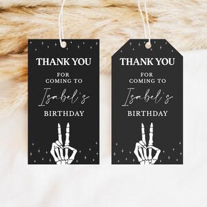 May include: Two black gift tags with white text and a skeleton hand making a peace sign. The tags read "THANK YOU FOR COMING TO Isabel's BIRTHDAY". The tags are rectangular and hexagonal.