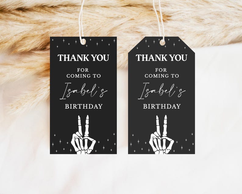 May include: Two black gift tags with white text and a skeleton hand making a peace sign. The tags read "THANK YOU FOR COMING TO Isabel's BIRTHDAY". The tags are rectangular and hexagonal.