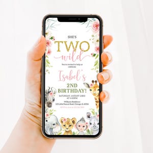 May include: A smartphone displays a birthday invitation with the text "She's Two Wild" in gold glitter font. The invitation features floral accents, animal illustrations, and details for Isabel's 2nd birthday.