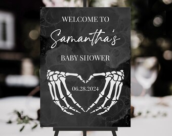 May include: A rectangular black sign with a white marble-like ink wash pattern. The text reads WELCOME TO Samantha's BABY SHOWER. Below the text is a white graphic of two skeleton hands forming a heart shape with the date 06.28.2024 printed inside.