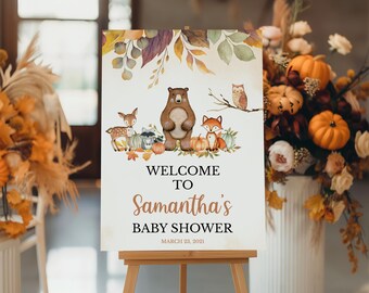 May include: A rectangular sign featuring watercolor illustrations of a bear, deer, fox, raccoon, and owl surrounded by autumn leaves and pumpkins. The text reads: WELCOME TO Samantha's BABY SHOWER MARCH 23, 2021. The sign is displayed on a wooden easel.
