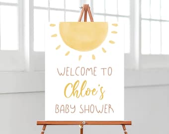 May include: Welcome to Chloe's Baby Shower sign with a yellow sun graphic. The sign is on an easel.