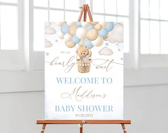 Peut inclure: Une pancarte de bienvenue pour une fête prénatale de couleur bleue et beige avec un ours en peluche dans un ballon à air chaud. La pancarte indique "We can bearly wait" et "Welcome to Maddison's Baby Shower 03.28.2023".