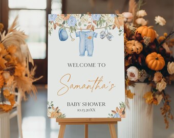 Puede incluir: Un letrero de bienvenida para un baby shower sobre un caballete. El letrero presenta una ilustración de acuarela de ropa de bebé y el texto "Welcome to Samantha's Baby Shower 10.13.20XX". El letrero está decorado con detalles florales en tonos azules, naranjas y crema.