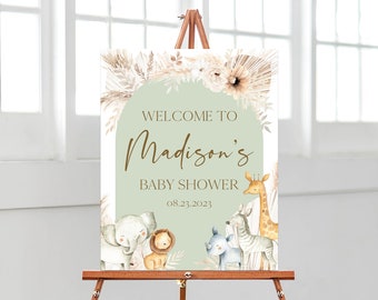 May include: A welcome sign for a baby shower with a green background and a white arch. The text reads "Welcome to Madison's Baby Shower 08.23.2023". The sign is decorated with illustrations of a giraffe, zebra, elephant, and lion.