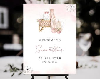 May include: A baby shower welcome sign featuring a watercolor illustration of pumpkins, a crib, and a spiderweb. The sign reads "Welcome to Samantha's Baby Shower 08-23-2024" in elegant script and serif fonts, set against a soft pink background.