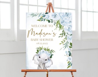 May include: A rectangular welcome sign for a baby shower featuring a watercolour illustration of a baby elephant wearing a blue floral crown. The text reads WELCOME TO Madison's BABY SHOWER 08.23.2023 in gold and brown lettering with blue roses.