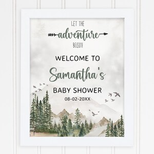 May include: A white framed print with a watercolor illustration of a mountain range with a forest in the foreground. The text "Let the adventure begin!" is at the top of the print, followed by "Welcome to Samantha's Baby Shower 08-02-20XX".
