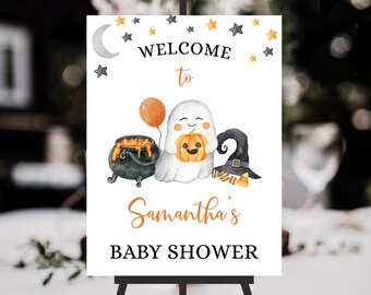 May include: A white rectangular sign featuring the text WELCOME to Samantha's BABY SHOWER. The design includes a watercolor ghost holding a pumpkin, a black cauldron with orange liquid, a black witch hat, an orange balloon, and stars.