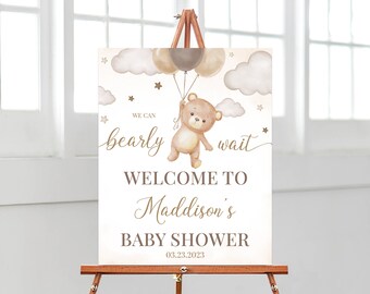 May include: A rectangular sign featuring a watercolor illustration of a brown teddy bear holding three balloons, surrounded by clouds and stars. The text reads: WE CAN bearly wait WELCOME TO Maddison's BABY SHOWER 03.23.2023 in brown and gold.