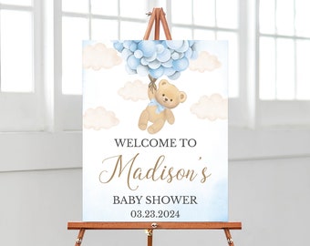 Pode incluir: Bem-vindo ao chá de bebê de Madison. O cartaz tem um fundo azul e branco em aquarela. Um urso de pelúcia está segurando balões azuis e flutuando nas nuvens. A data do chá de bebê é 03.23.2024.