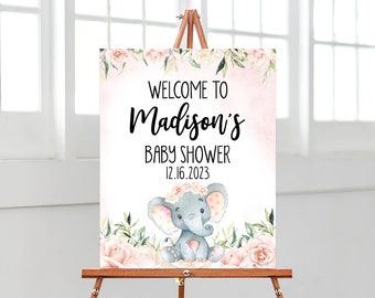 May include: A baby shower sign on a wooden easel. The sign reads "Welcome to Madison's Baby Shower 12.16.2023" in black script. A watercolor illustration of a gray elephant with a floral crown is at the bottom, surrounded by pink roses and green leaves.