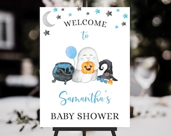 Könnte beinhalten: Ein weißes Schild auf einer schwarzen Staffelei mit den Worten "WELCOME to" in schwarzer und blauer Schrift. Das Schild zeigt eine Aquarellillustration eines Geistes, der einen Kürbis, einen Kessel und einen Hexenhut hält. Der Text "Samantha's BABY SHOWER" steht ebenfalls auf dem Schild.