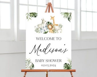 May include: A rectangular welcome sign for a baby shower featuring watercolor illustrations of a zebra, rhino, lion, giraffe, and elephant surrounded by green tropical leaves. The text reads: WELCOME TO Madison's BABY SHOWER 02.03.2024.