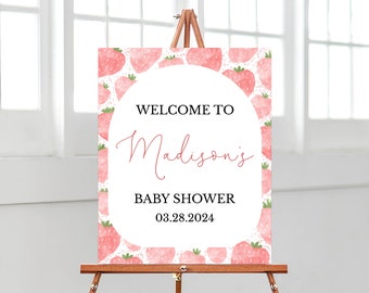 May include: A rectangular welcome sign featuring a watercolor strawberry pattern border and a central white arch. The text reads: WELCOME TO Madison's BABY SHOWER 03.28.2024. The sign is displayed on a wooden easel stand.