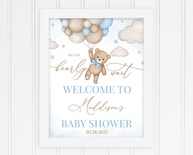 May include: A framed baby shower sign with a watercolor design. The sign features a teddy bear holding balloons, with the text "We can bearly wait" and "Welcome to Maddyson's Baby Shower" in blue and gold script. The date is 03.28.2023.