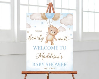 Pode incluir: Um cartaz de boas-vindas para um chá de bebê azul e marrom com um urso de desenho animado segurando balões. O cartaz diz "We can bearly wait" e "Welcome to Maddison's Baby Shower 03.23.2023".