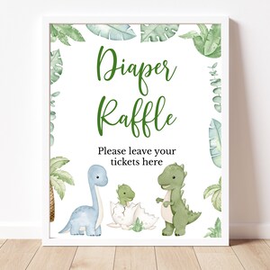 May include: A white sign with green leaves and dinosaurs. The sign says "Diaper Raffle" and "Please leave your tickets here".