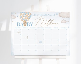 Può includere: Un calendario per baby shower blu e bianco con un orsacchiotto in mongolfiera. Il calendario è intitolato "Indovina l'arrivo di Baby Nathan" e ha date dal 23 aprile al 27 maggio.